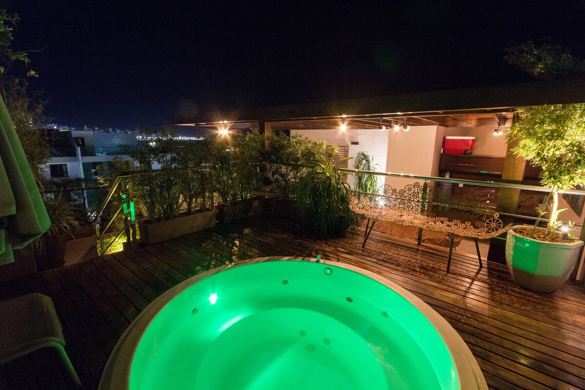 Ein Whirlpool auf einer Holzterrasse bei Nacht, beleuchtet mit Lichterketten und umgeben von Topfpflanzen.