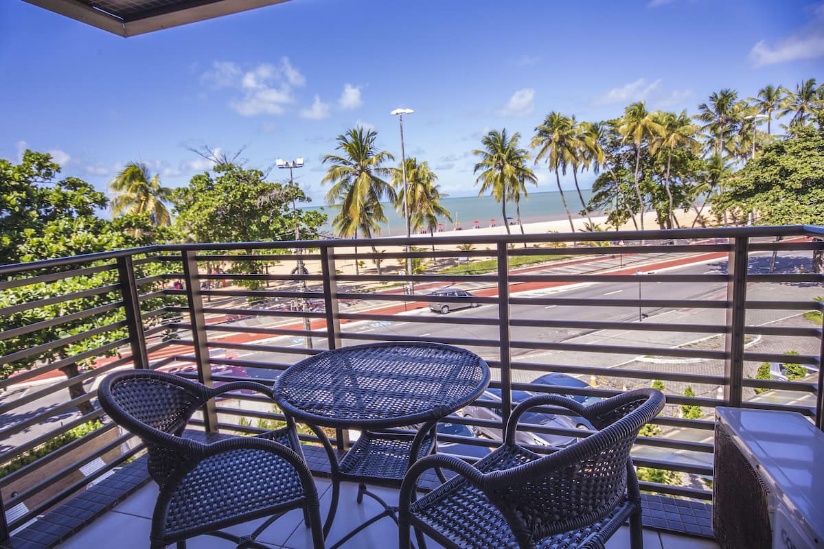 A balcony with wicker furniture and a view of the beach and palm trees.