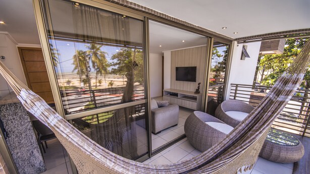 Ein modernes Wohnzimmer mit einem großen Glasfenster, das auf einen Balkon führt, einer Hängematte und einem Flachbildfernseher.