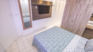 Un dormitorio con cama, un armario de madera, un espejo y una pequeña estantería con luz.