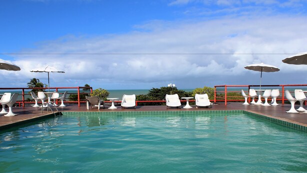 Zona de piscina con sillones y sombrillas, con vista a una masa de agua.