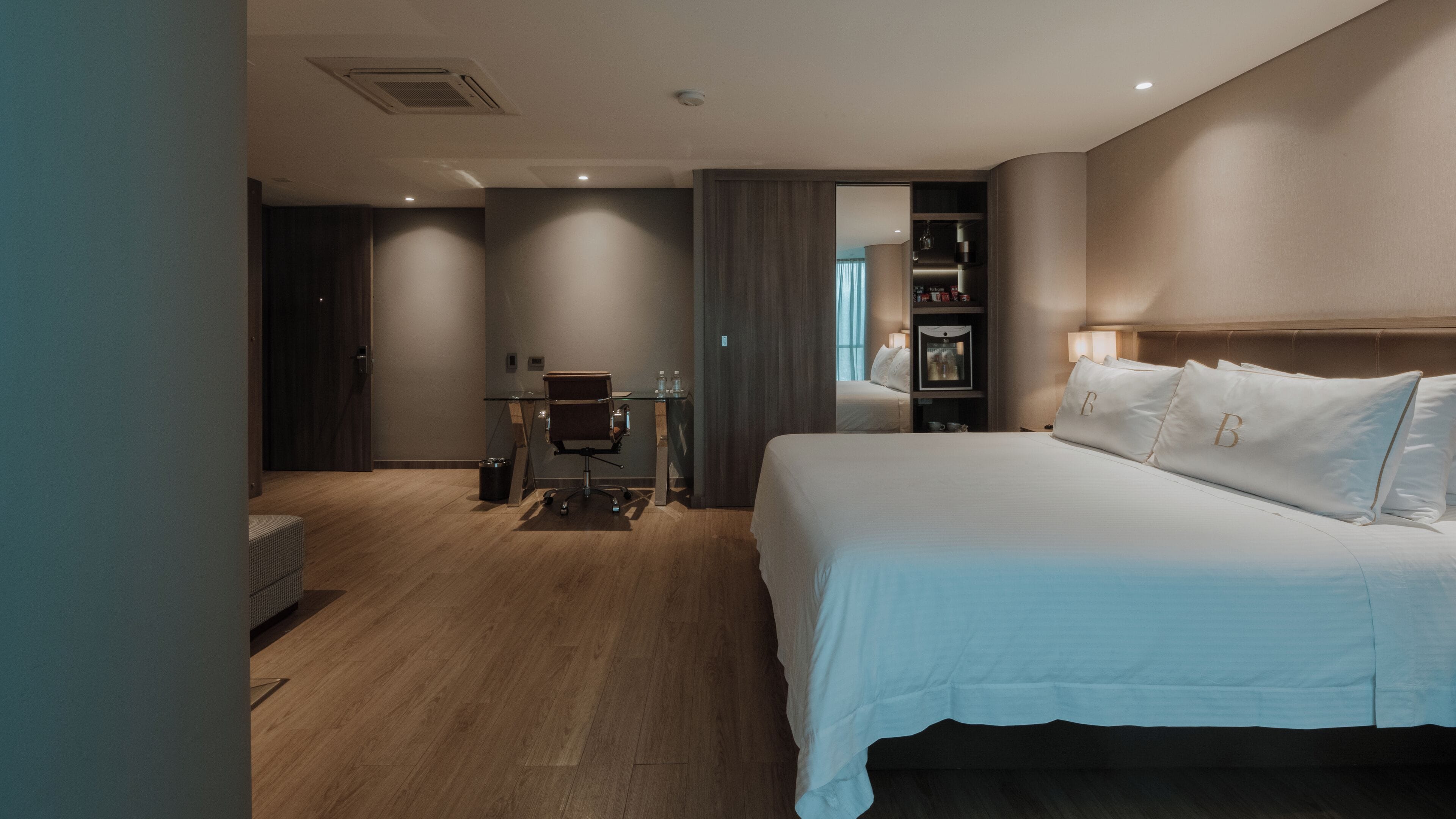 A modern hotel room with a large bed, a desk, and a wardrobe.