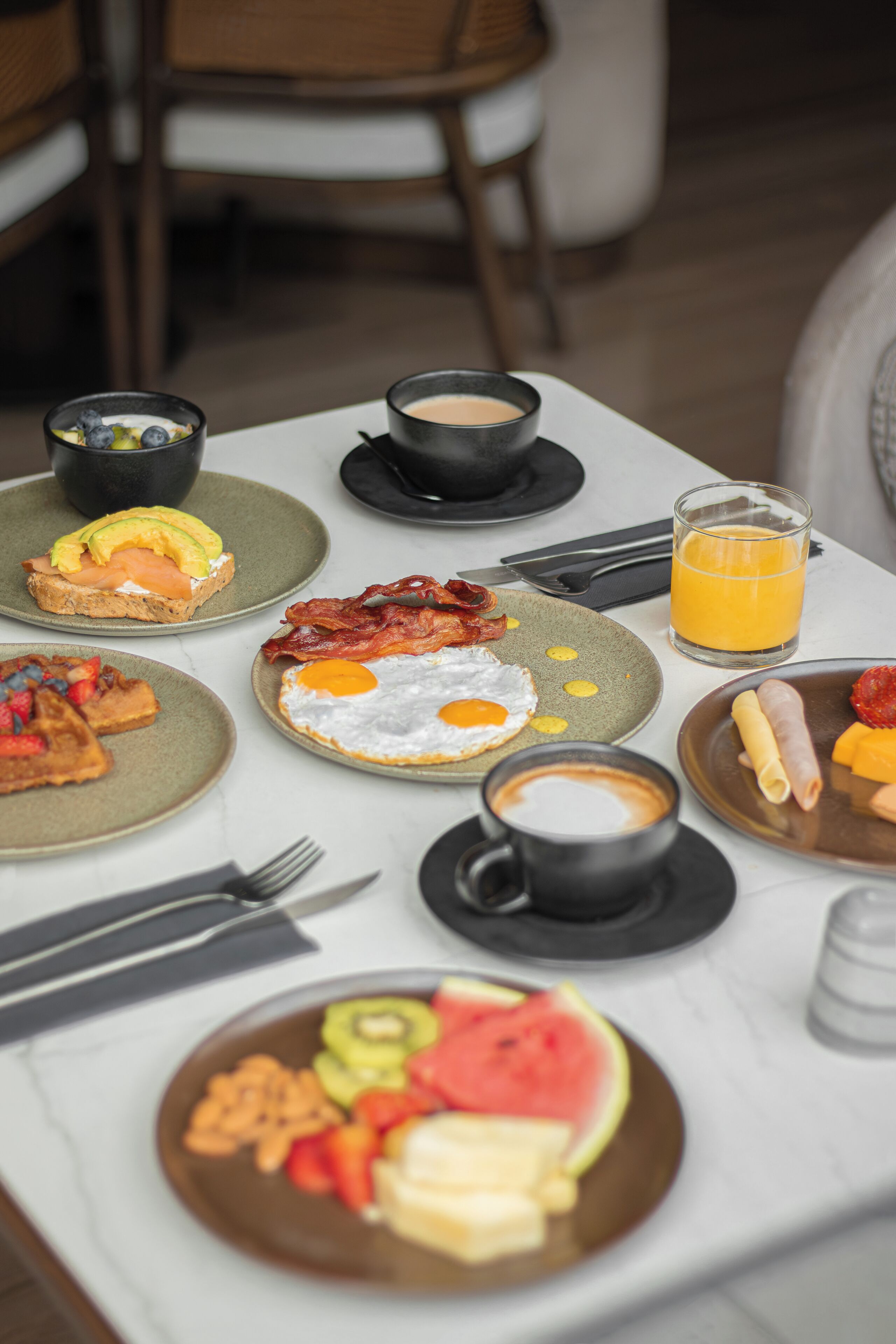 A breakfast table with plates of food, a glass of orange juice, and a cup of coffee.