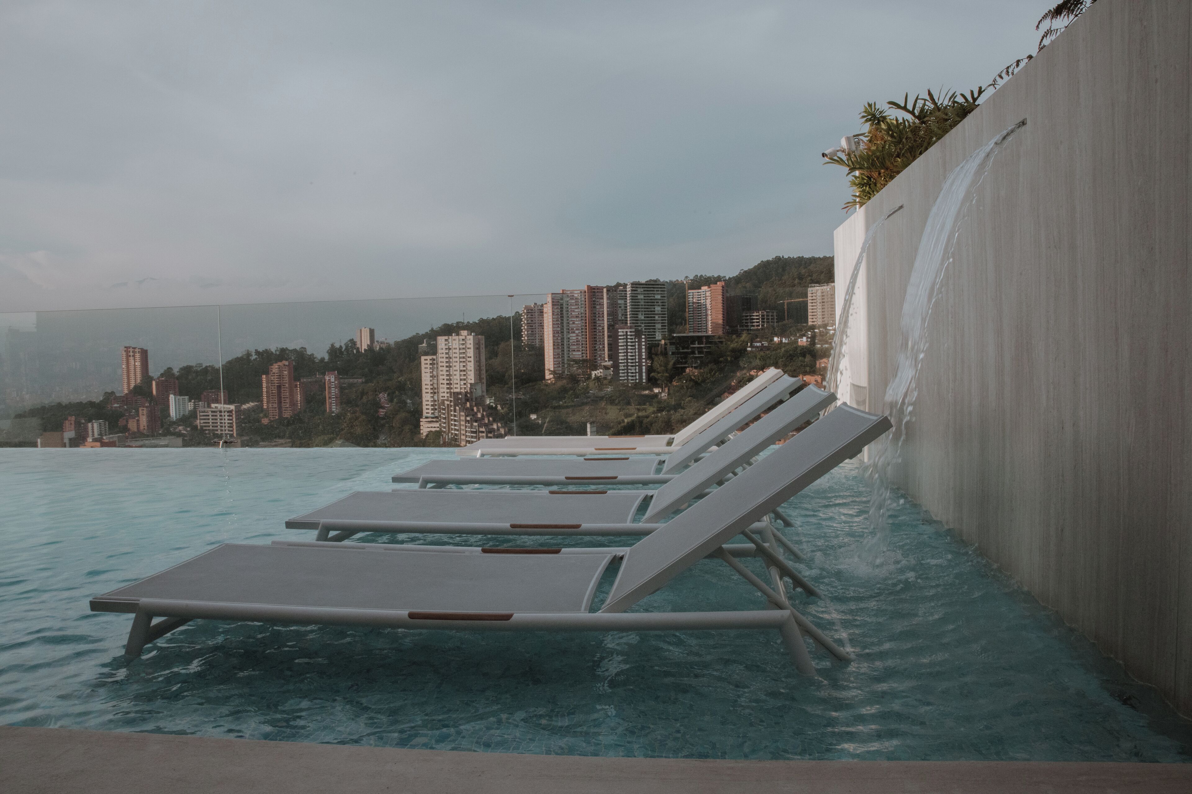 Un espace aménagé au bord de la piscine, avec des chaises longues et une vue sur le paysage urbain en arrière-plan.