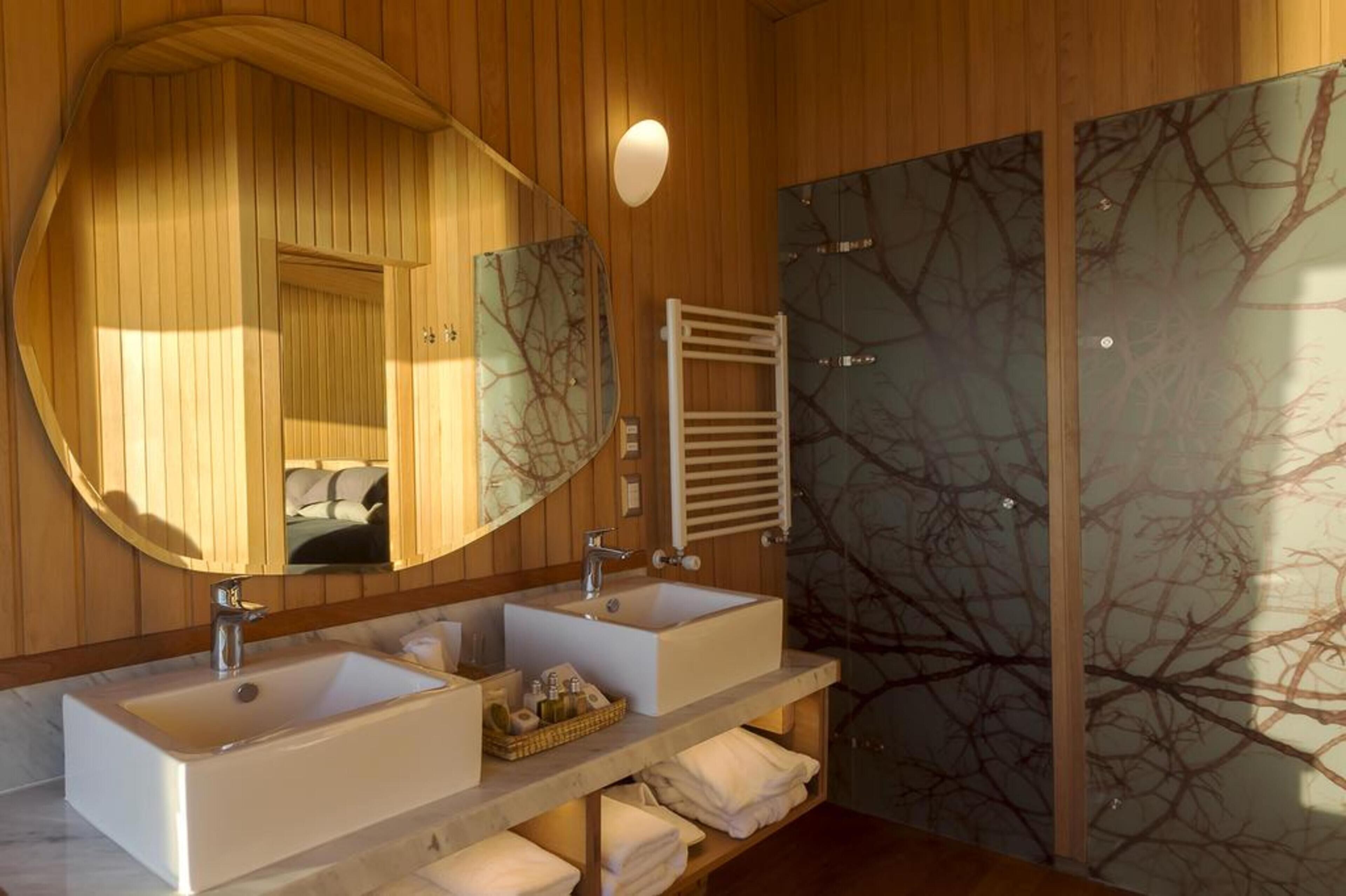 A modern bathroom with two sinks, a large mirror, and a glass shower enclosure.