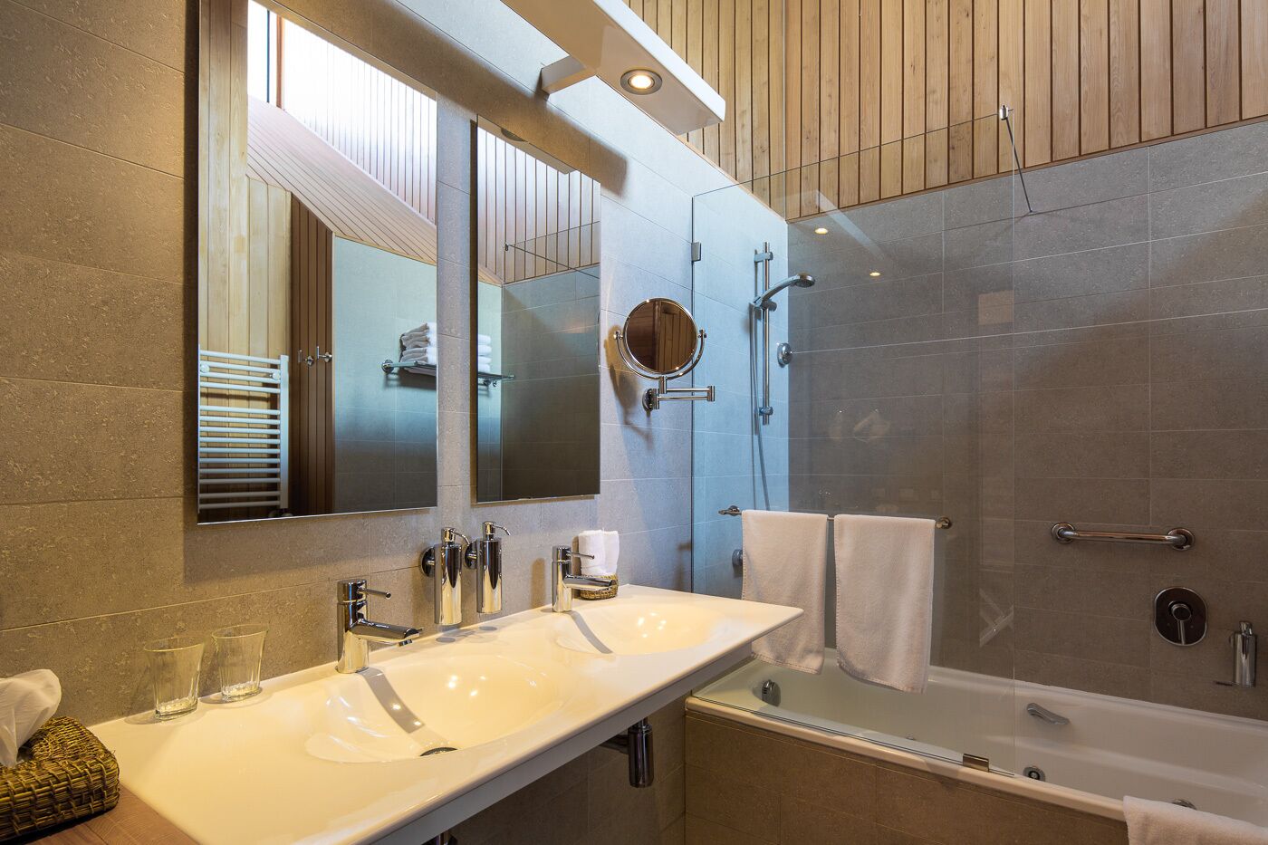 A modern bathroom with a large mirror, two sinks, a bathtub, and a glass-enclosed shower.