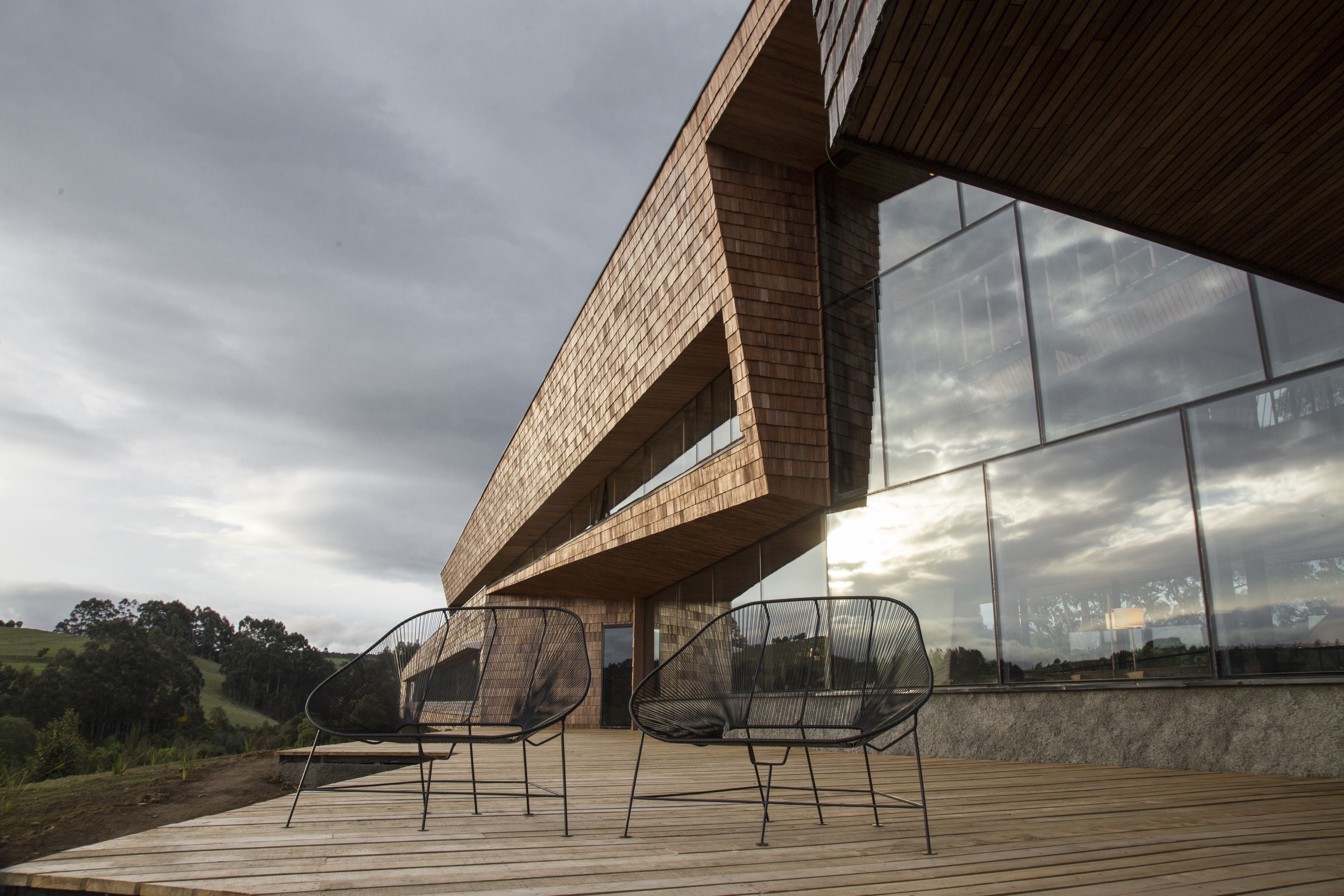 Un edificio moderno con una terraza de madera y dos sillas negras.
