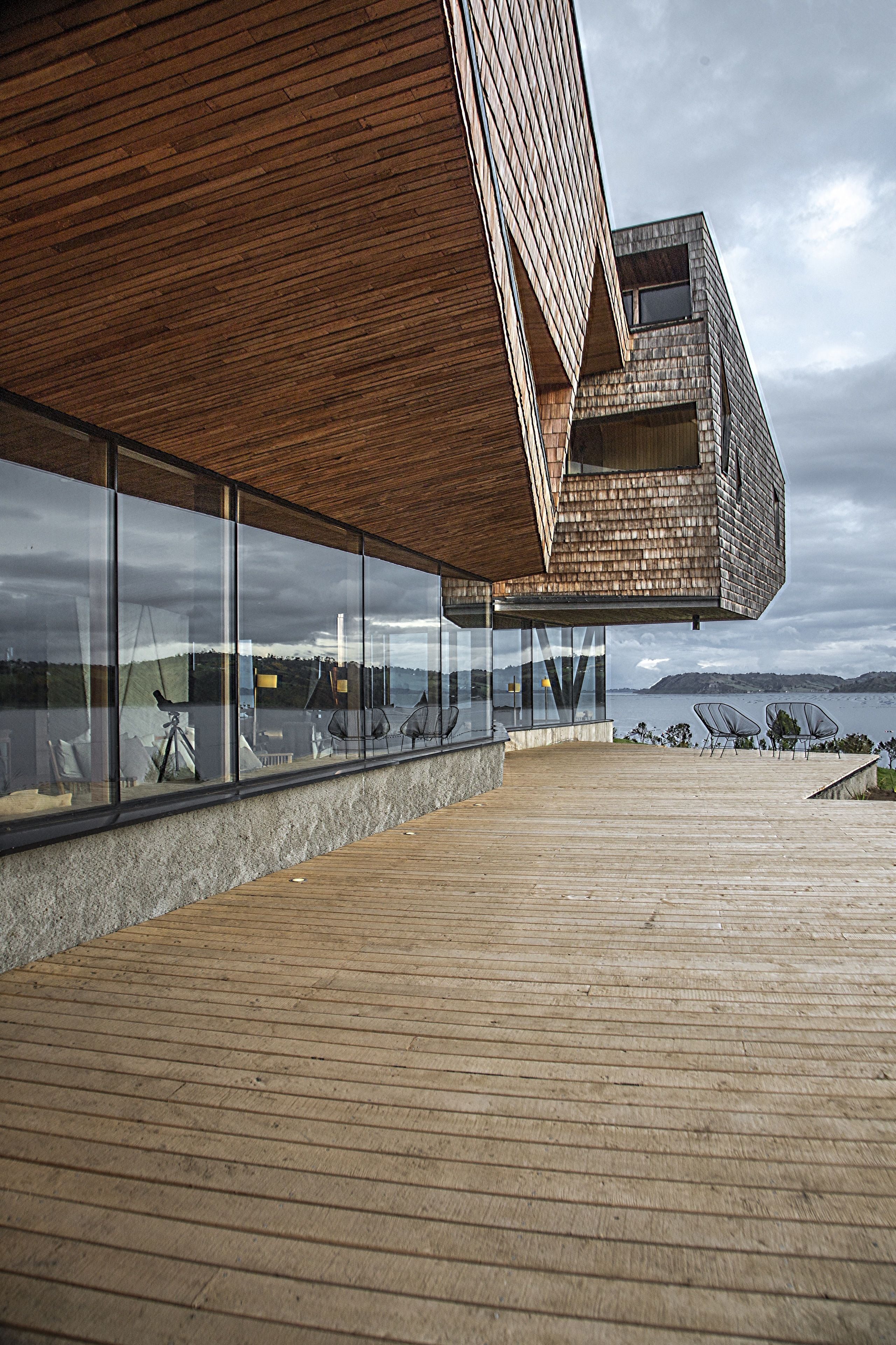 Un edificio moderno con terraza de madera y amplios ventanales con vistas al agua.
