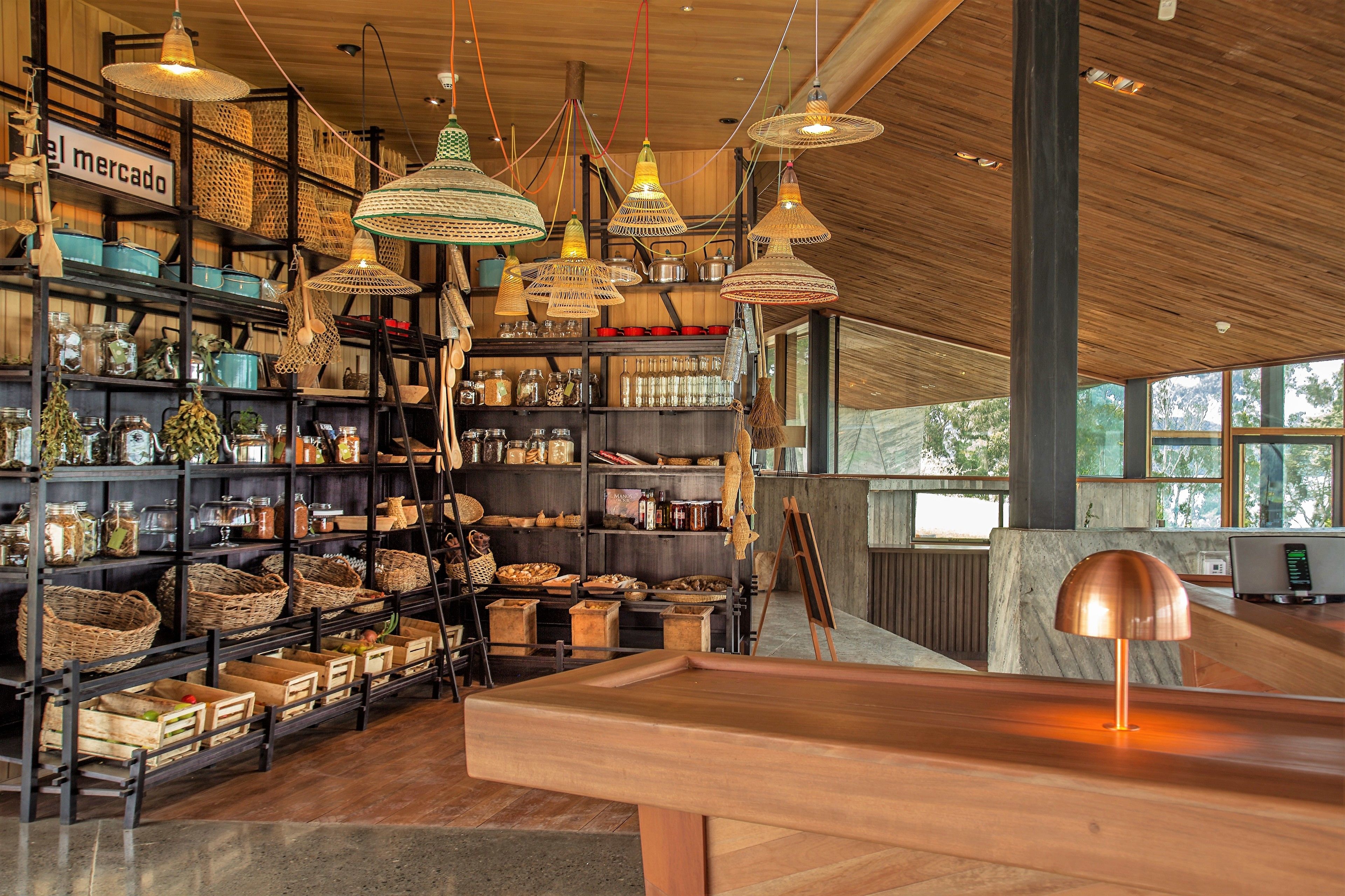 Un interior amplio con vigas de madera, estantes llenos de cestas y frascos, y una gran mesa de madera con una lámpara.