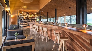 A modern bar area with wooden bar stools, a long counter, and pendant lighting. - Refugia Chiloé (Castro)