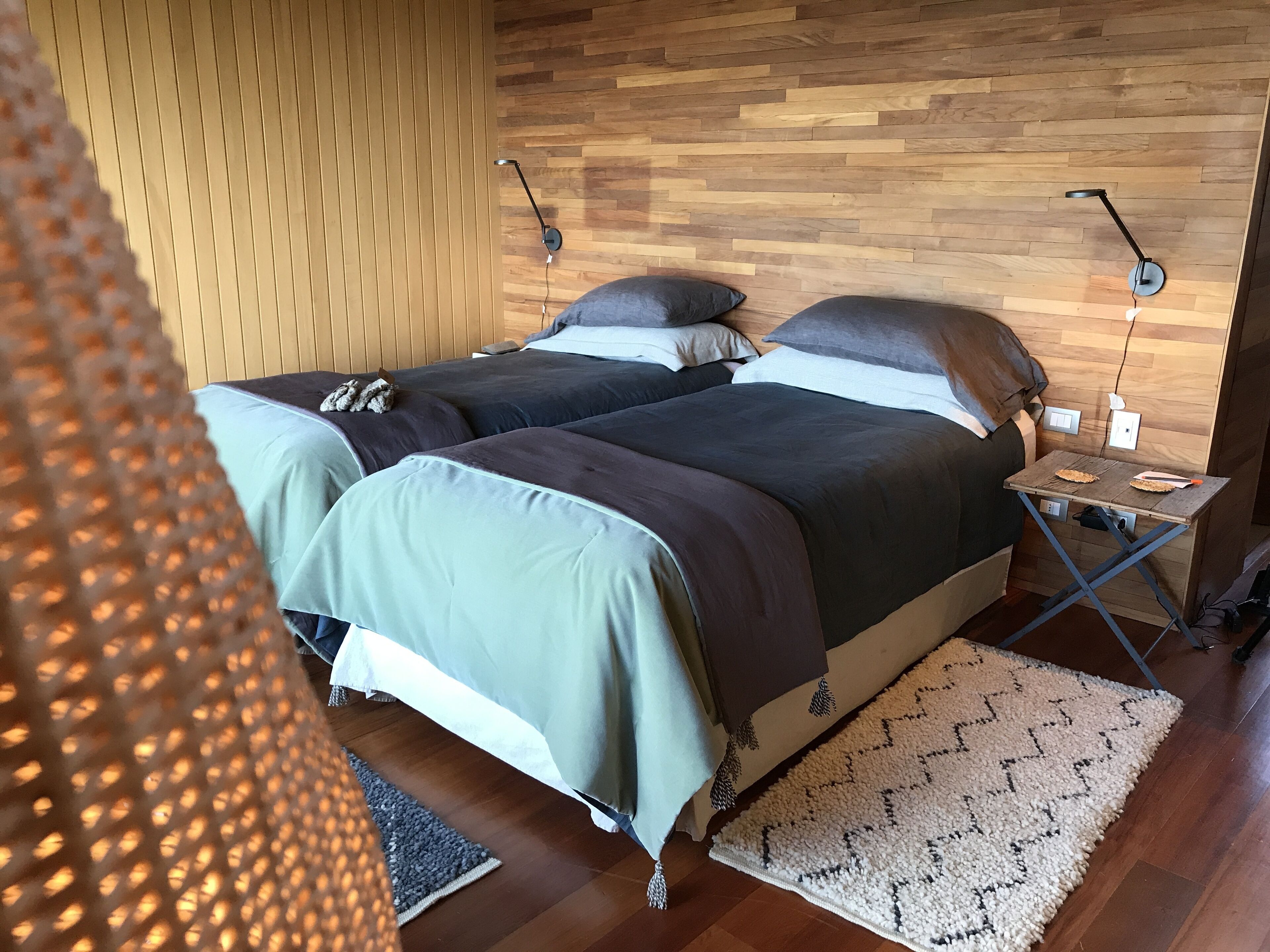 Ein Schlafzimmer mit zwei Betten, Holzwandverkleidung, einem kleinen Tisch und einem gemusterten Teppich.
