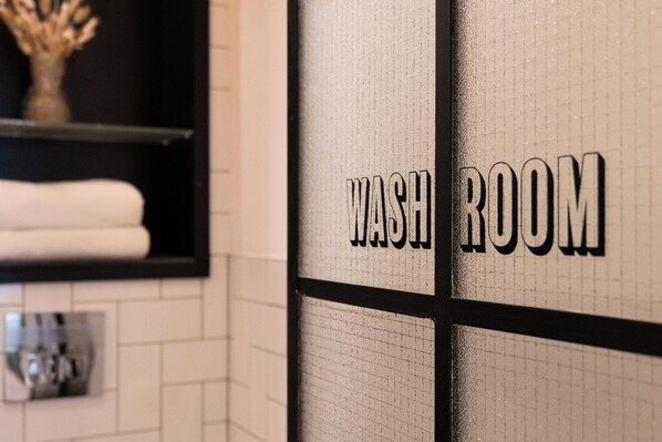 A washroom with a tiled wall and a shelf with towels. - Room2 London Hammersmith Townhouse (London)