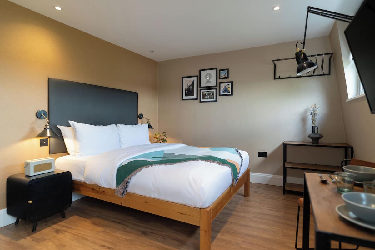 A bedroom with a wooden bed, bedside table with a lamp, a small table with bowls, and framed pictures on the wall.