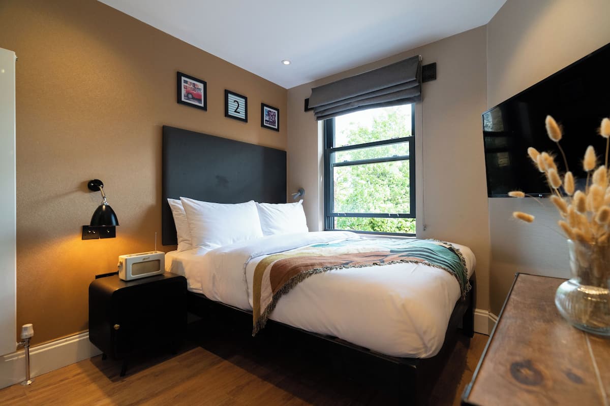 A bedroom with a bed, bedside table, lamp, and a TV on the wall.