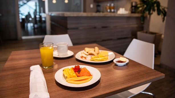 Uma mesa de madeira com pratos de comida, um copo de suco de laranja e um guardanapo.