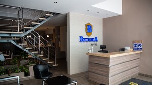 Uma área de recepção de hotel com uma escadaria moderna, um balcão de atendimento e um espaço para sentar.