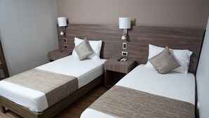 Duas camas de casal com estruturas de madeira e roupa de cama branca, cada uma com mesa de cabeceira e luminária.