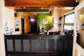 Una recepción con una persona sentada detrás, una pared verde y un techo de madera.