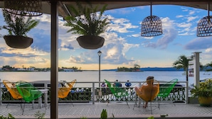 A terrace with chairs and potted plants, overlooking a body of water and a distant shoreline.