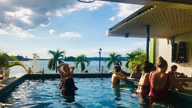 A swimming pool with people relaxing and a view of the sea.