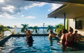 A swimming pool with people relaxing and a view of the sea. - Hotel Petén Express - Hostel (Flores)