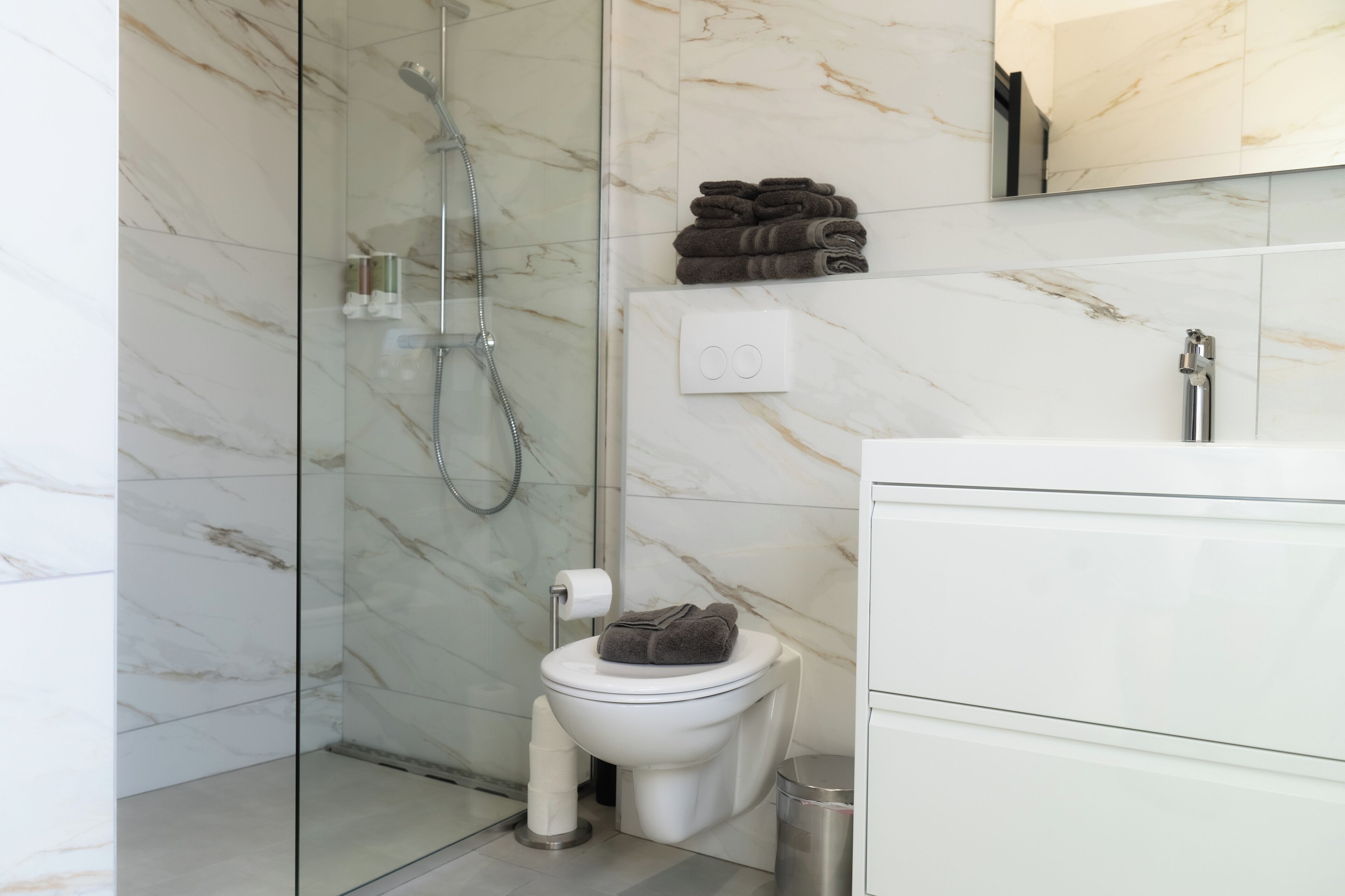A modern bathroom with a glass-enclosed shower, a toilet, and a sink with a mirror above.