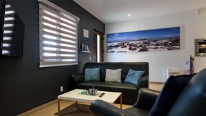 Un salon moderne avec un canapé en cuir noir, une table basse blanche et un grand tableau représentant un paysage de plage accroché au mur.