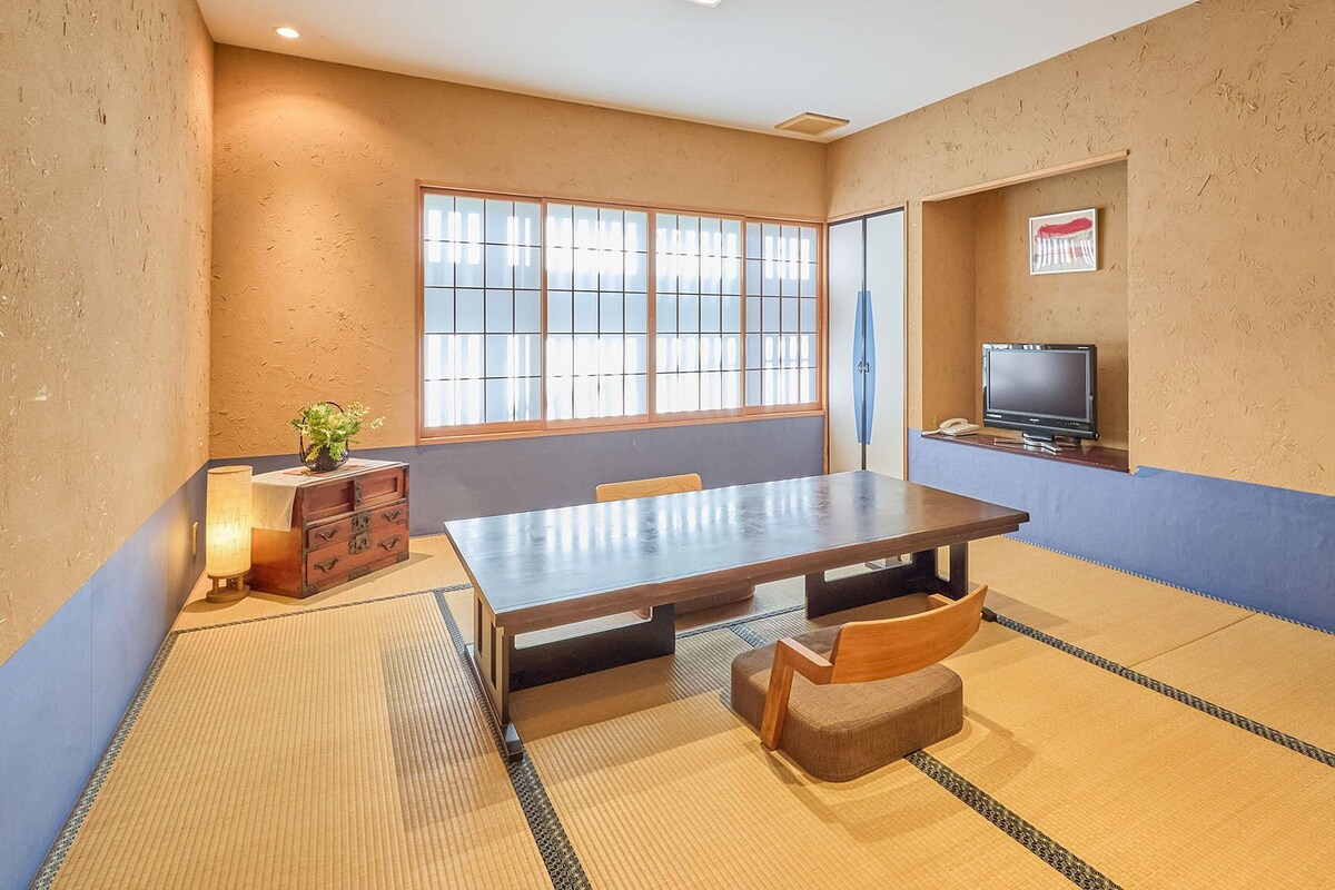 A room with tatami mats, a wooden table, a television, and a window with a view.