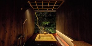 A wooden sauna with a rectangular hot tub, a shower area, and a view of trees through a glass partition. - Seikanso (Hakone)