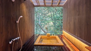 Interior de fusta amb banyera d'hidromassatge, dutxa i vista als arbres a través d'una finestra.