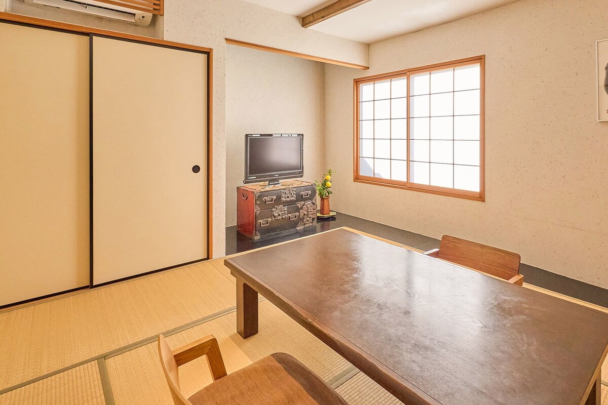 A traditional Japanese room with tatami flooring, a low table, and a television on a cabinet.
