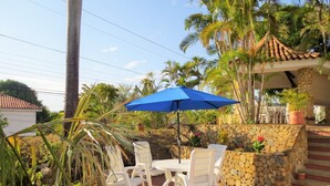 Un patio al aire libre con una mesa, sillas, un paraguas azul y un muro de piedra con plantas.