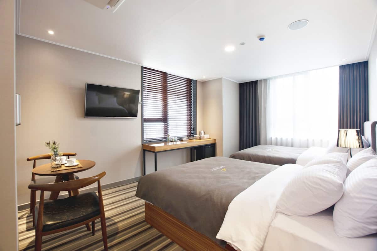 A hotel room with a bed, a desk, a chair, a television, and a window with blinds.