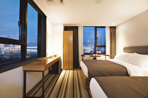 A hotel room with a large window, a desk, two beds, and a view of a cityscape. - GNB Hotel (Busan)