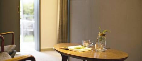 A room with a round wooden table, a chair, a small vase with a plant, and a glass of water.