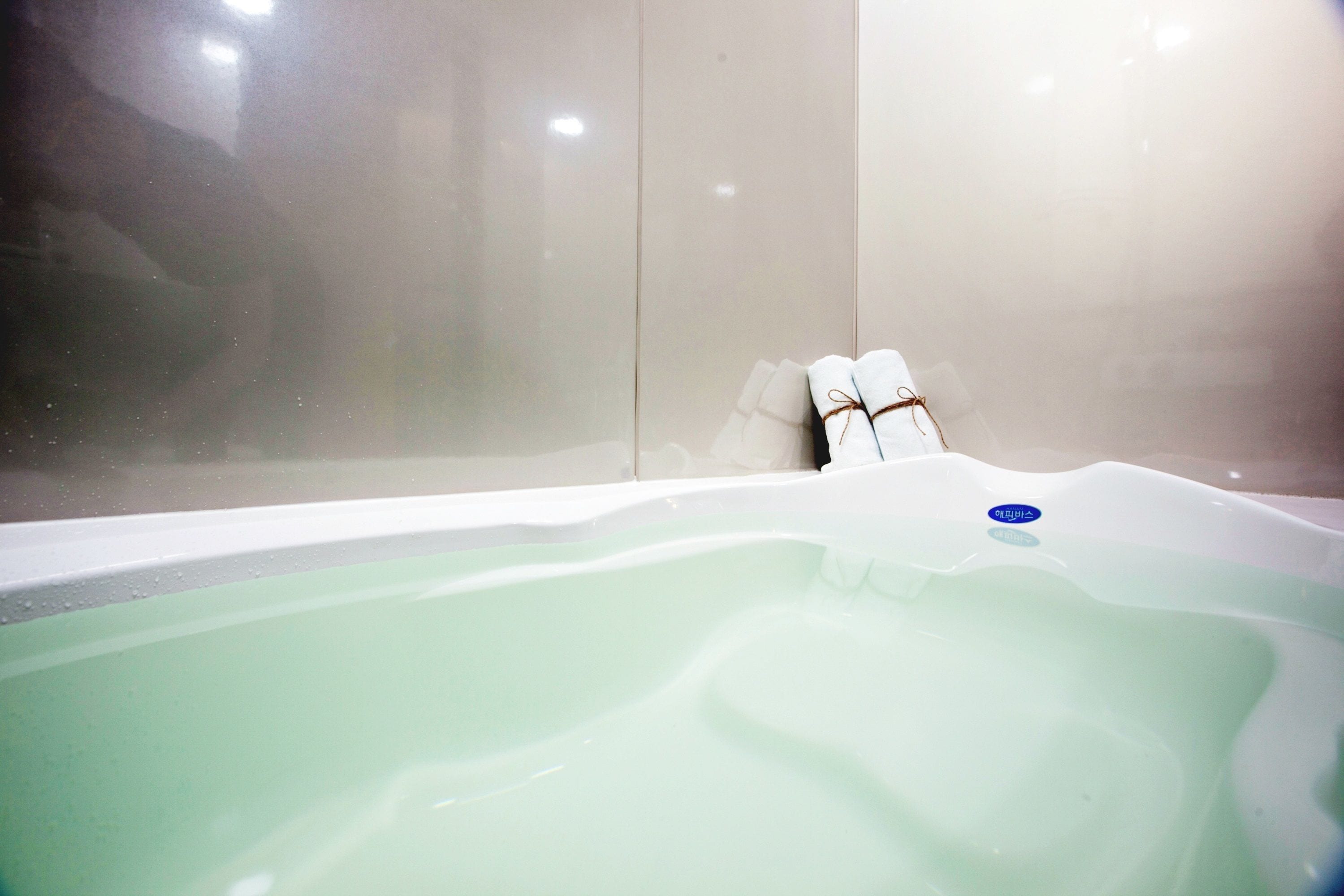 Une baignoire ornée d’un logo circulaire bleu, un porte-serviettes avec des serviettes et une paroi en verre.