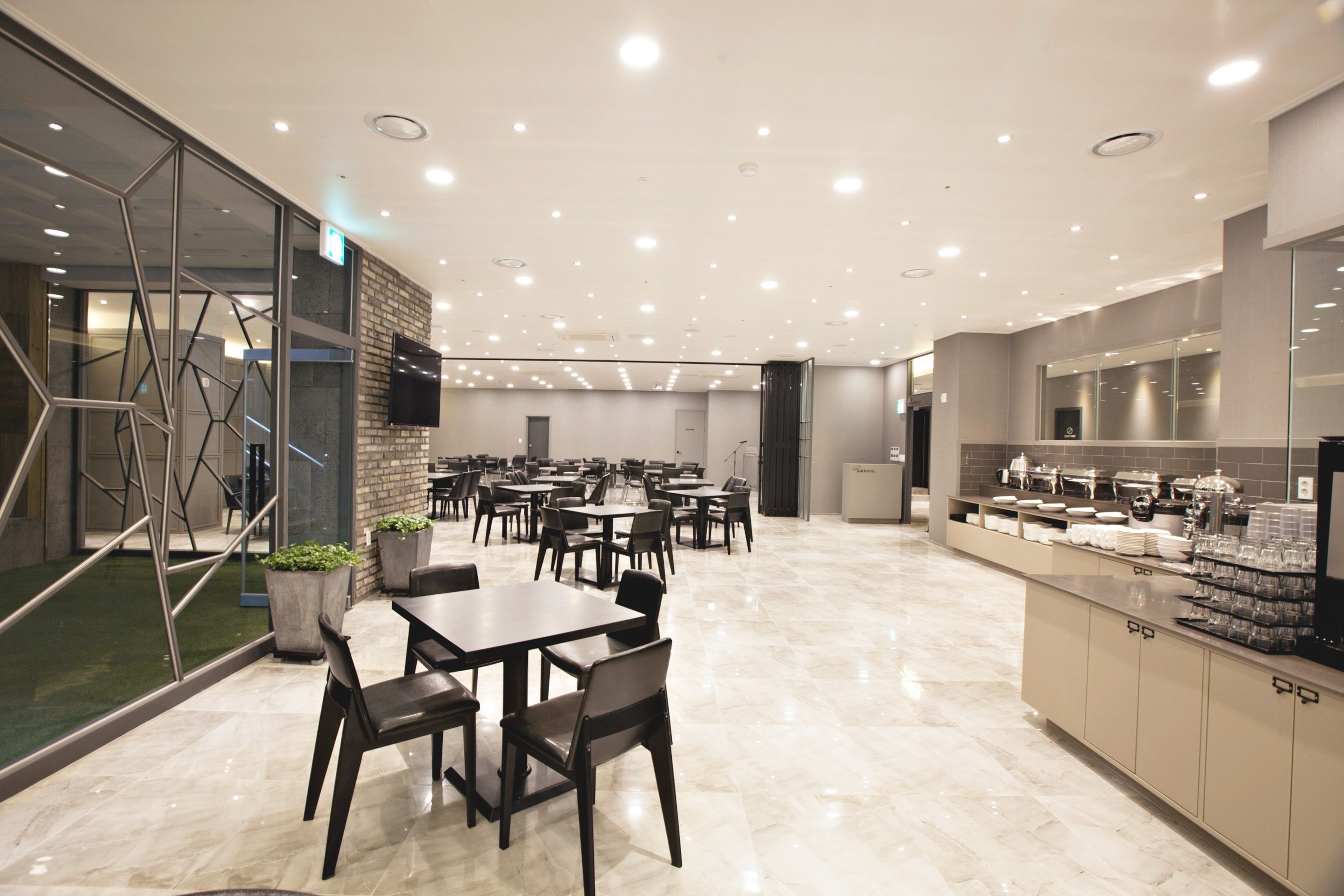 A modern dining area with multiple tables and chairs, a kitchen counter with various items, and a glass wall with a geometric design.