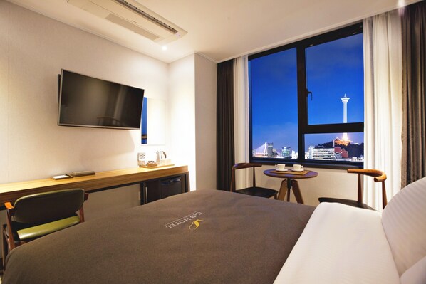 A hotel room with a bed, a desk, a chair, a TV, and a window with a city view.