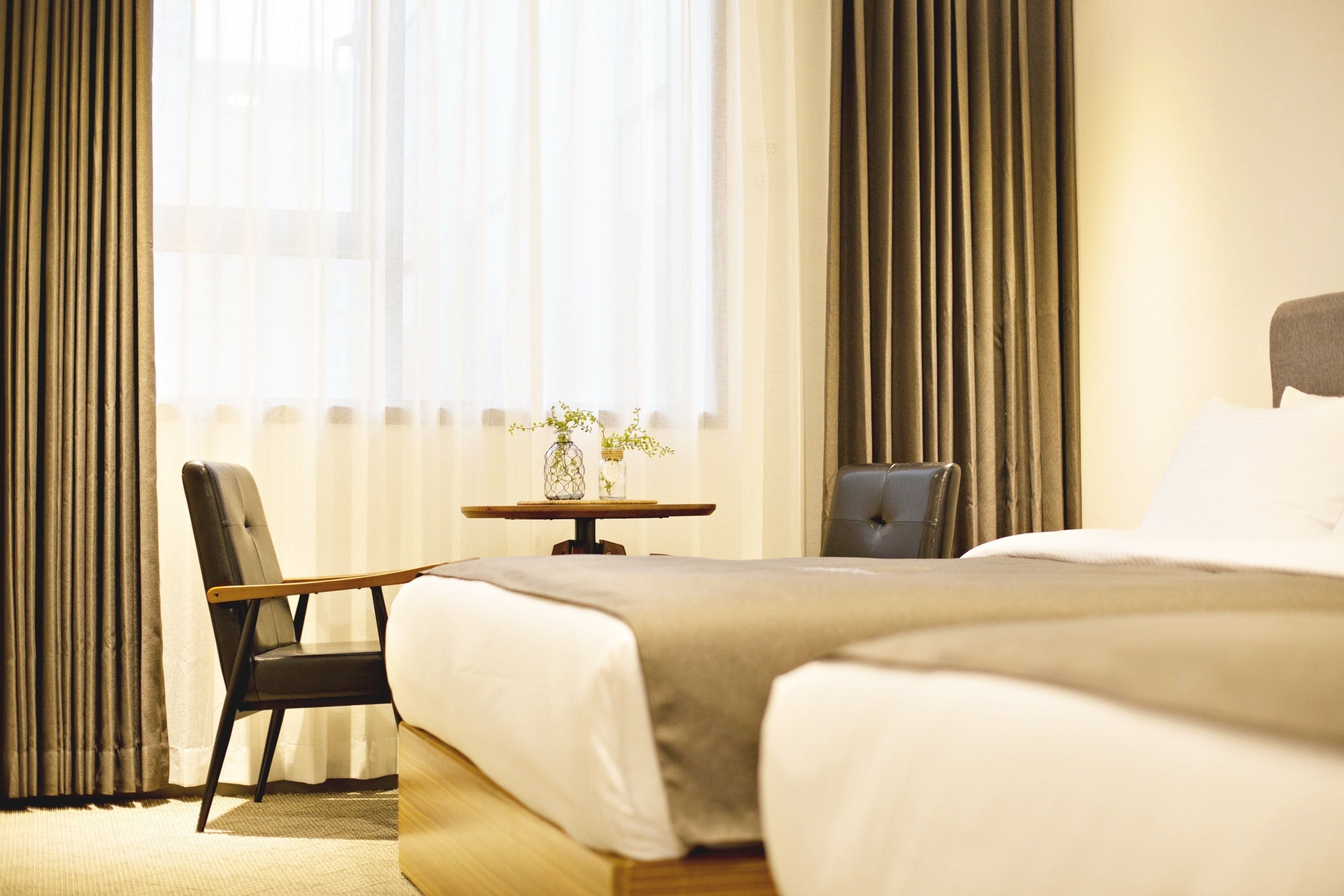 A hotel room with two beds, a small table with a vase, and a chair.