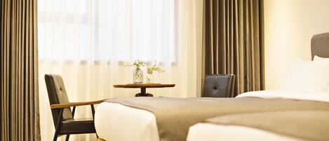 A hotel room with two beds, a small table with a vase, and a chair.