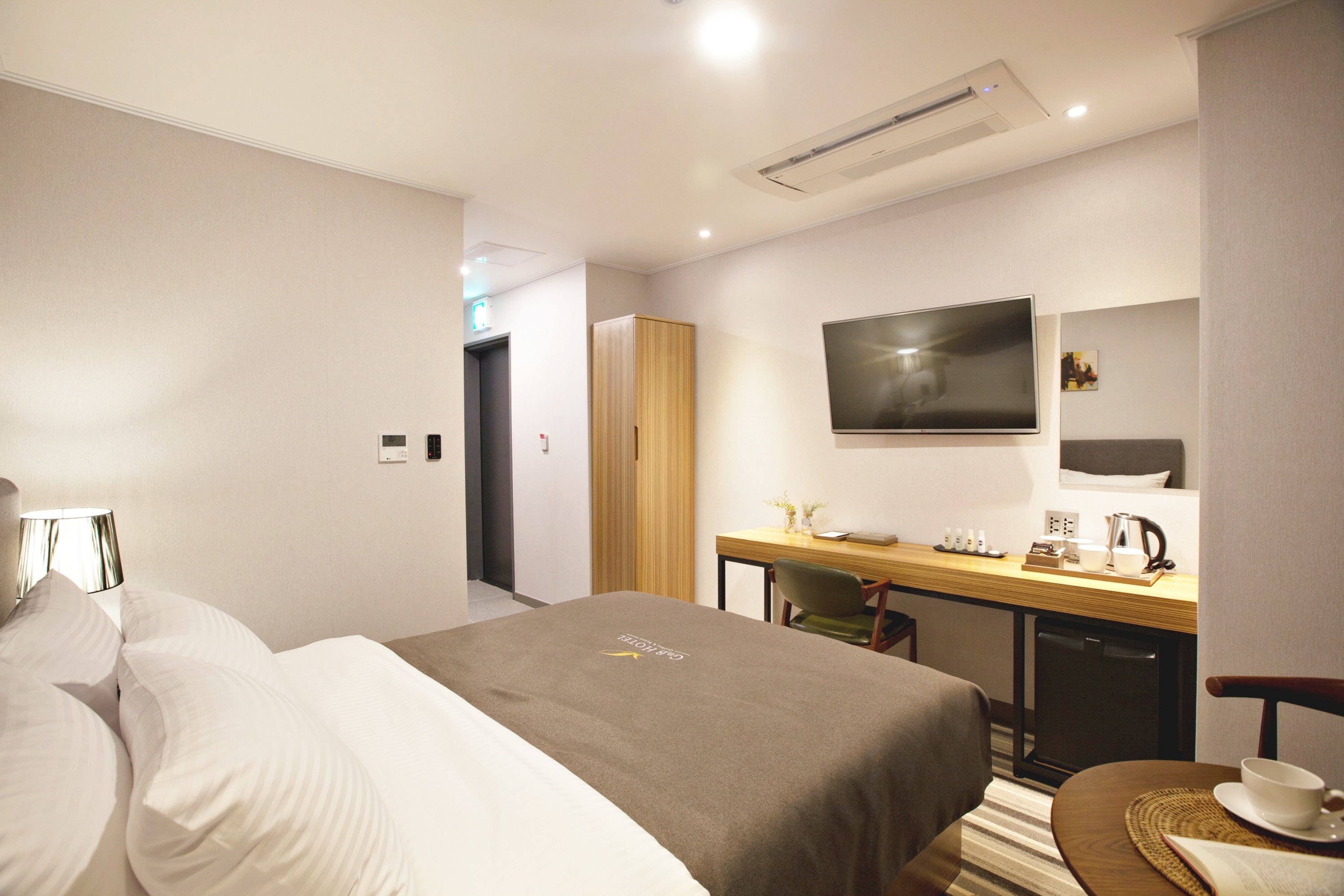 A hotel room with a bed, a desk with a chair, a television, and a small kitchenette.