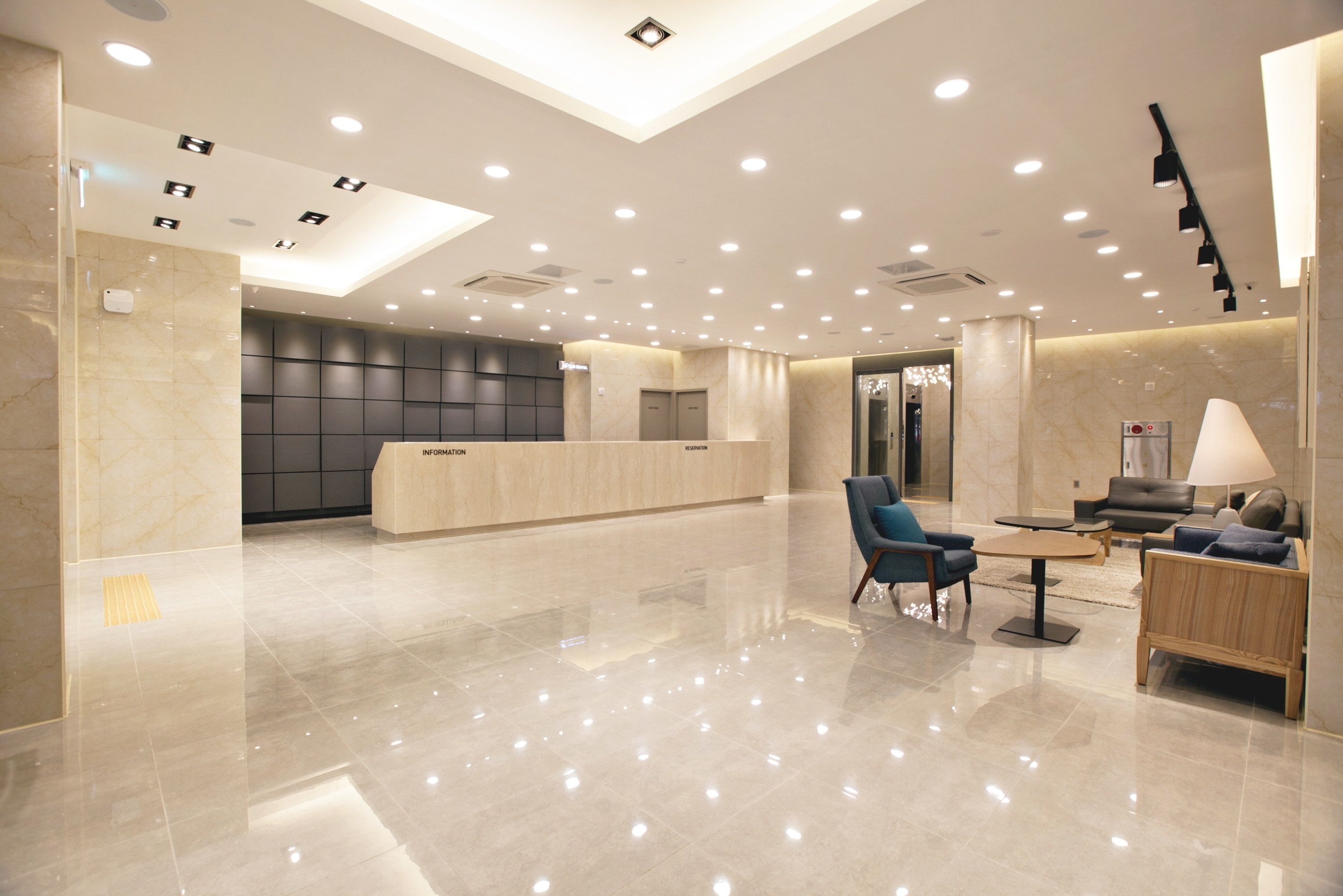 Een moderne hotellobby met een receptiebalie, een zithoek en een kroonluchter.