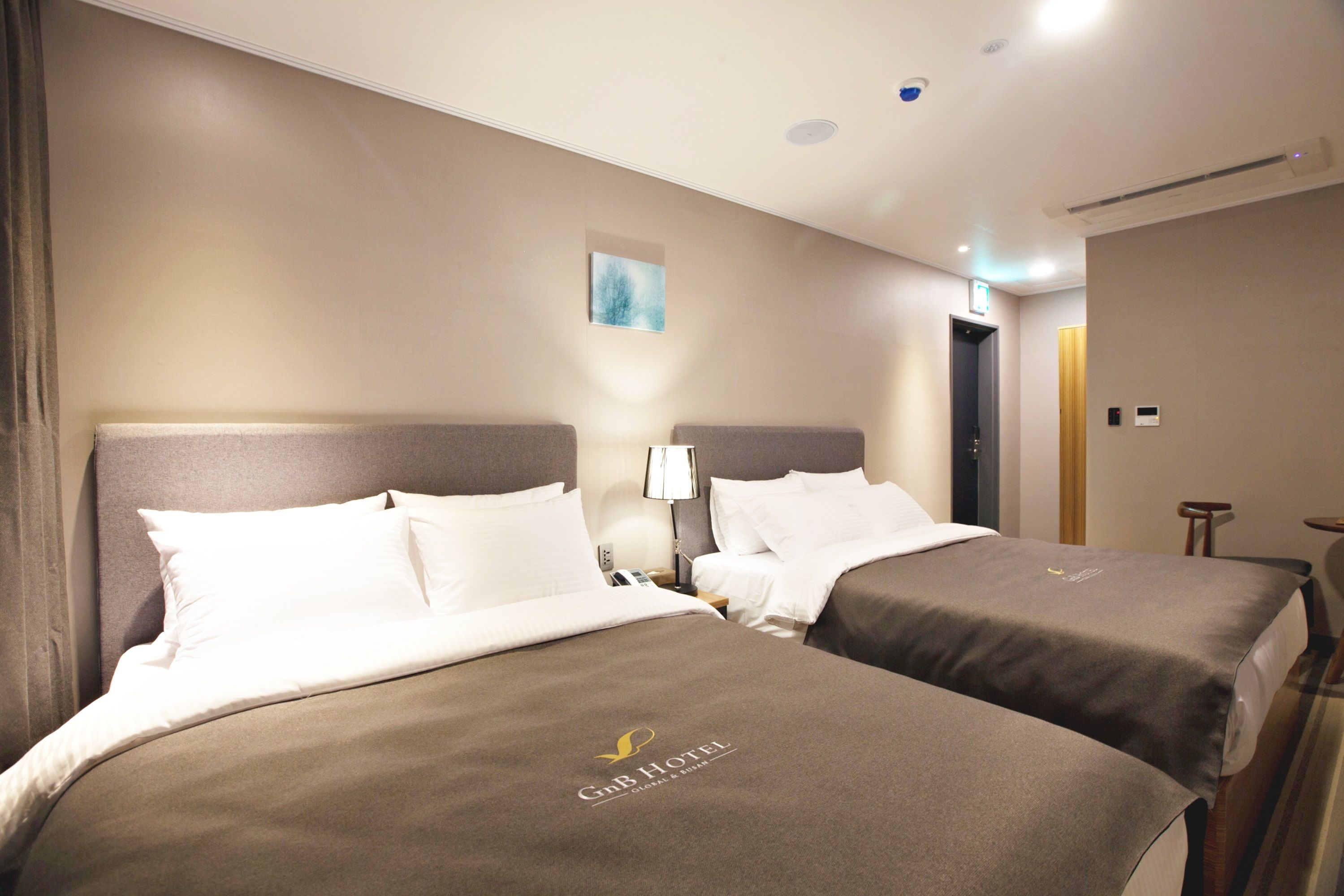 A hotel room with two beds, each with a headboard and pillows, a nightstand with a lamp, and a small table.