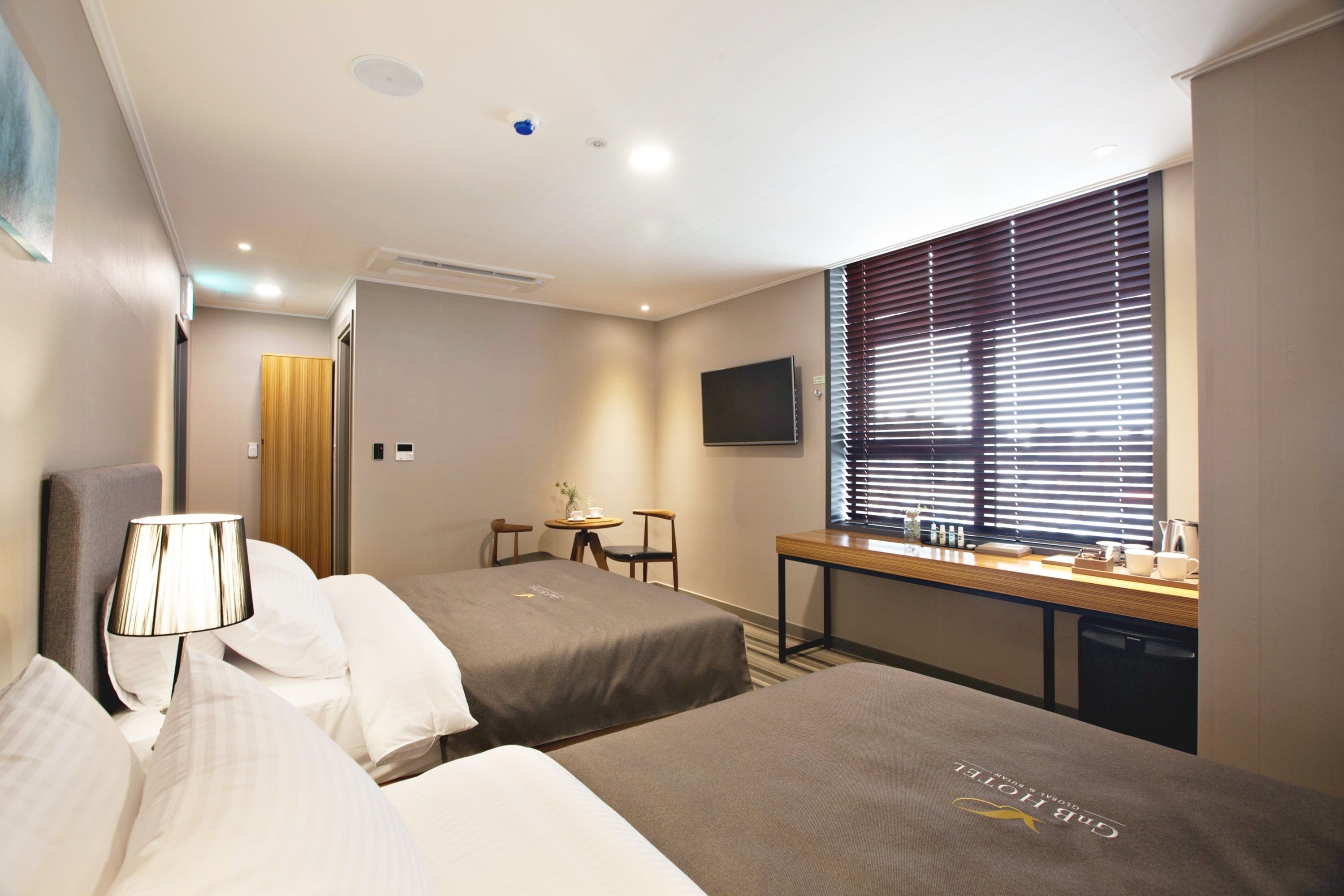 A hotel room with two beds, a desk, a chair, a TV, and a window with blinds.