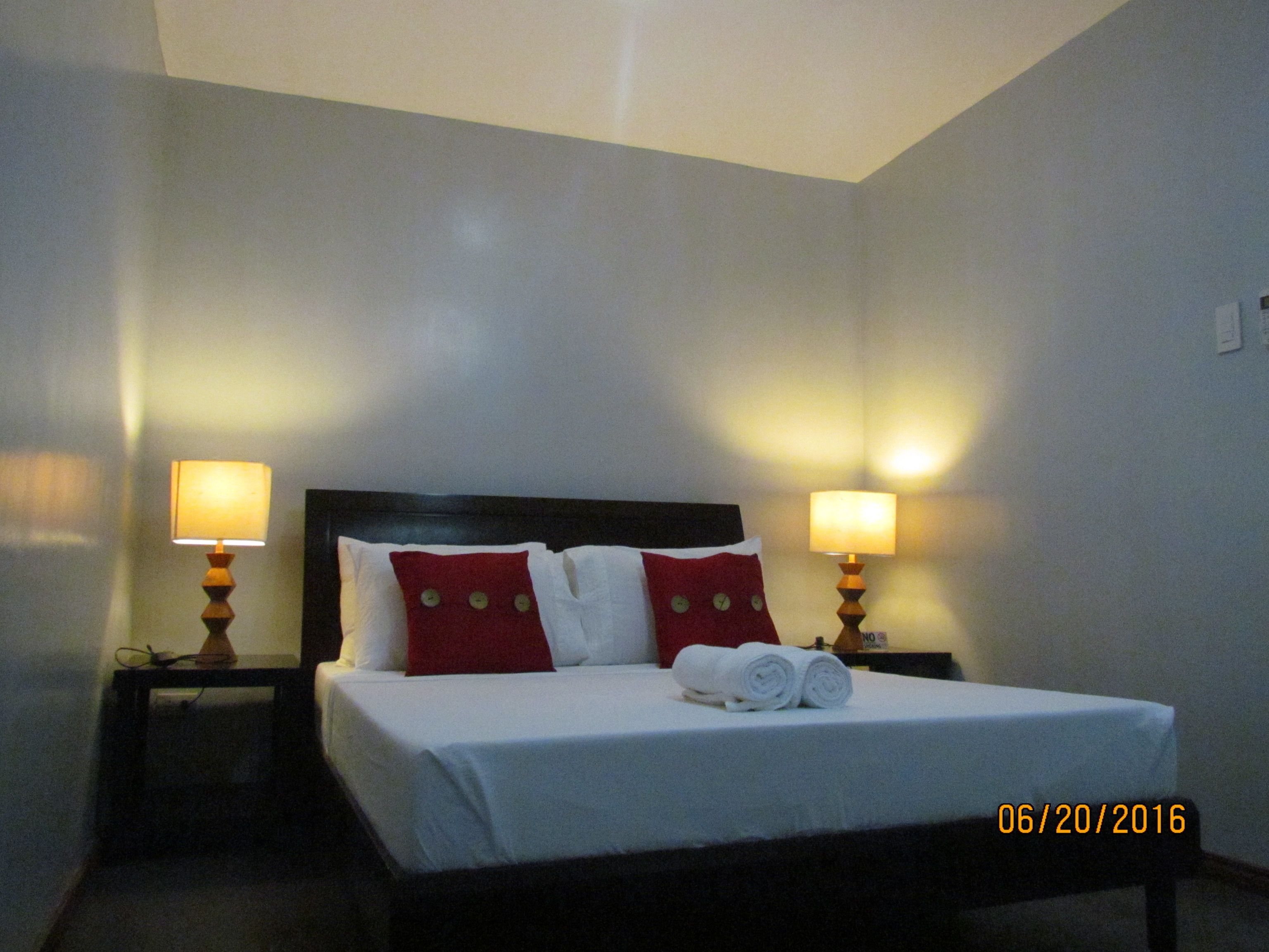 A hotel room with a bed, two bedside lamps, and a nightstand.