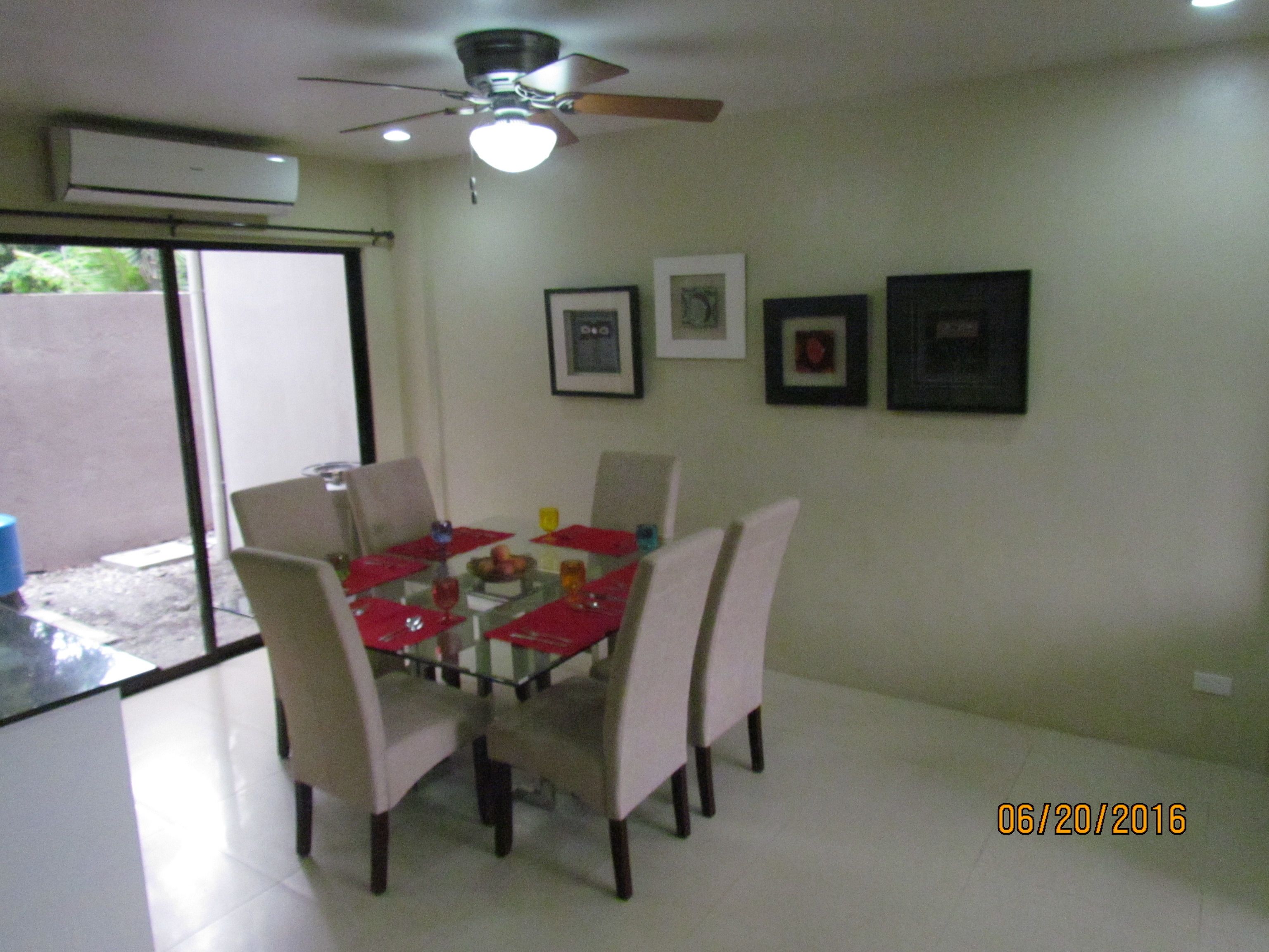 A dining area with a glass table, four chairs, and a ceiling fan.