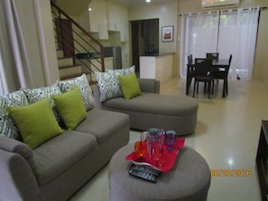 A living room with a sofa set, a dining table, and a kitchen area in the background.