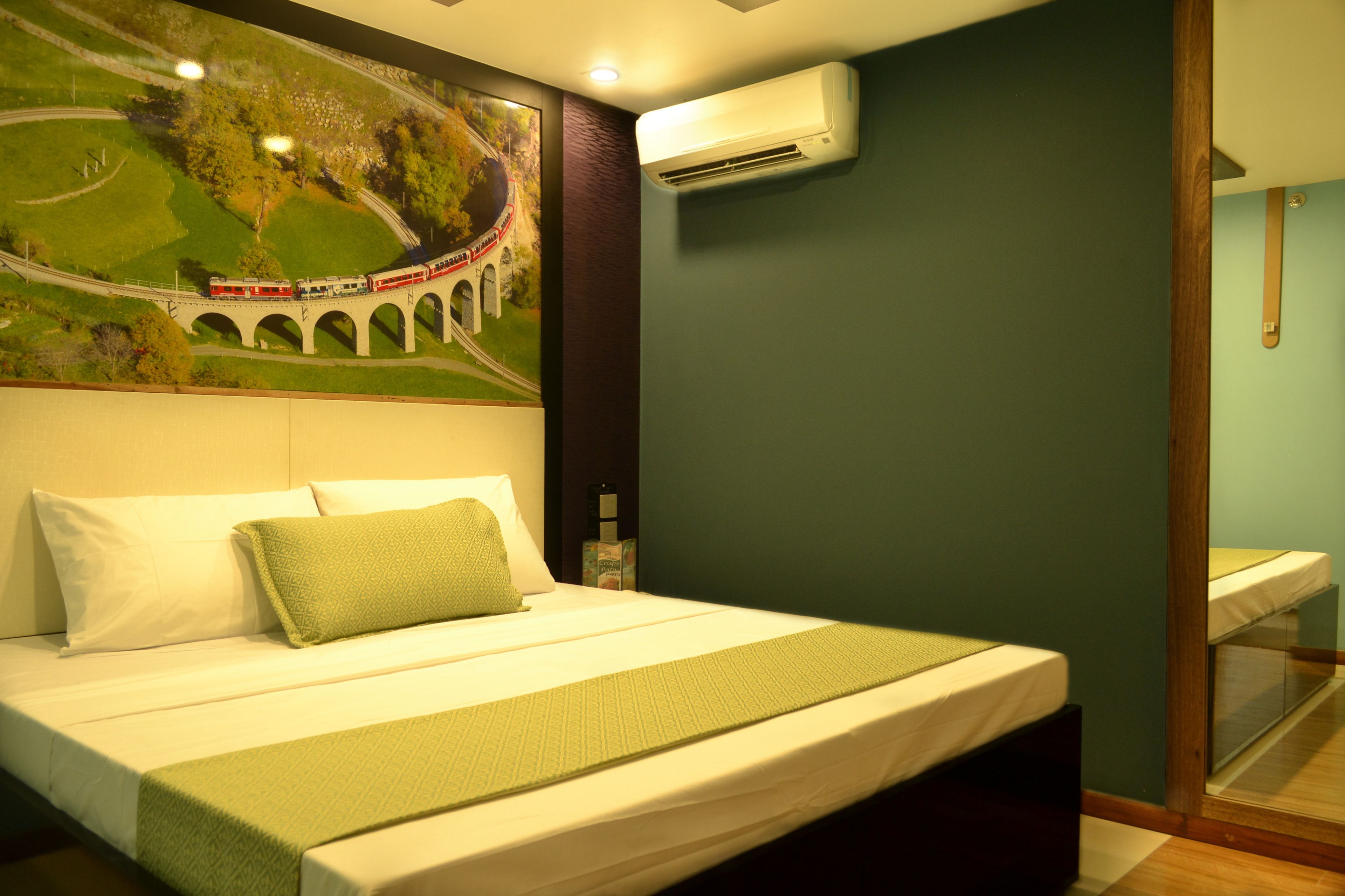 A neatly made bed with a green bedspread, a white pillow, and a green pillow. There is a wall-mounted air conditioner above the bed.