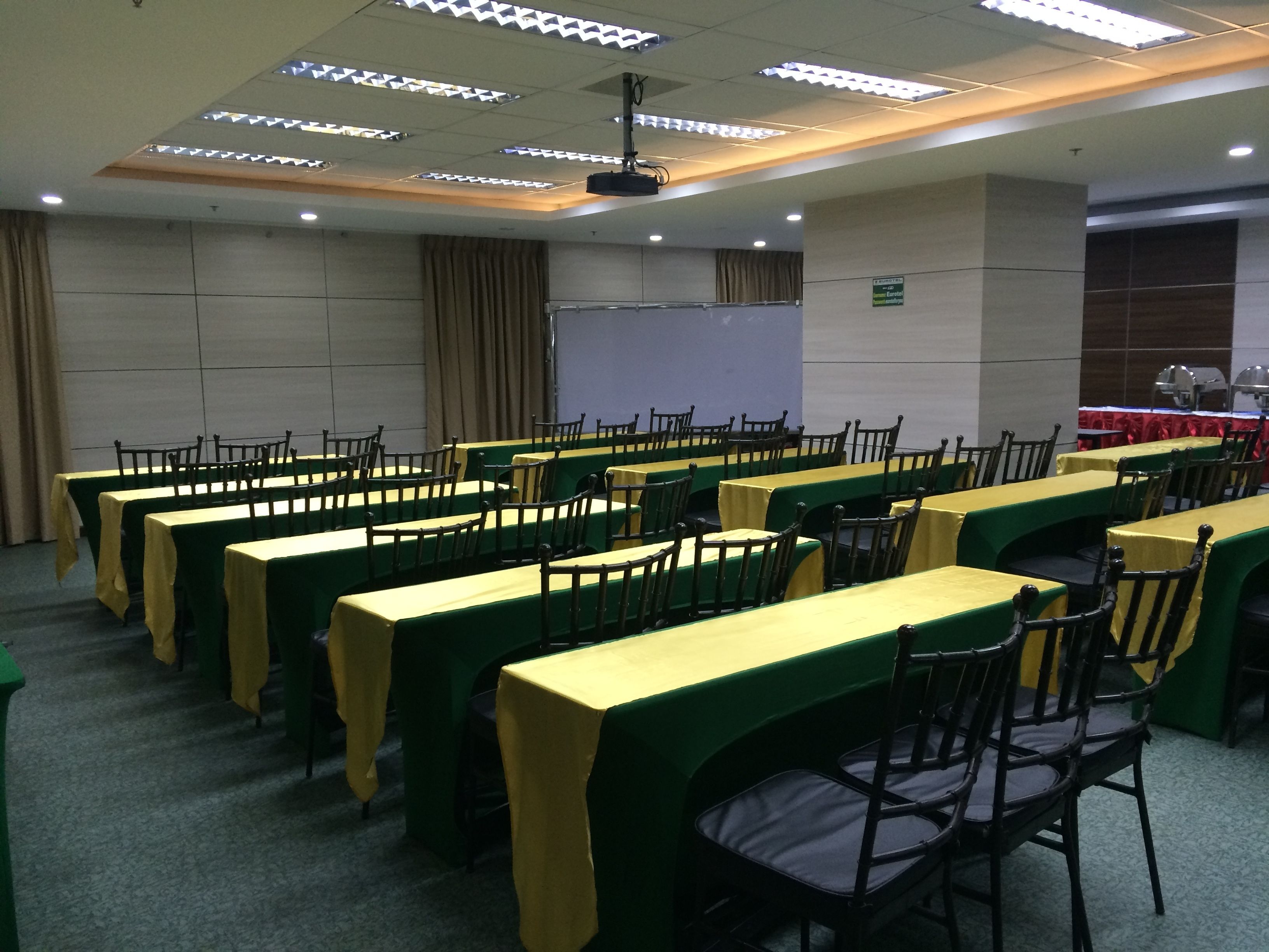 A conference room with rows of tables and chairs, a projector, and a whiteboard.