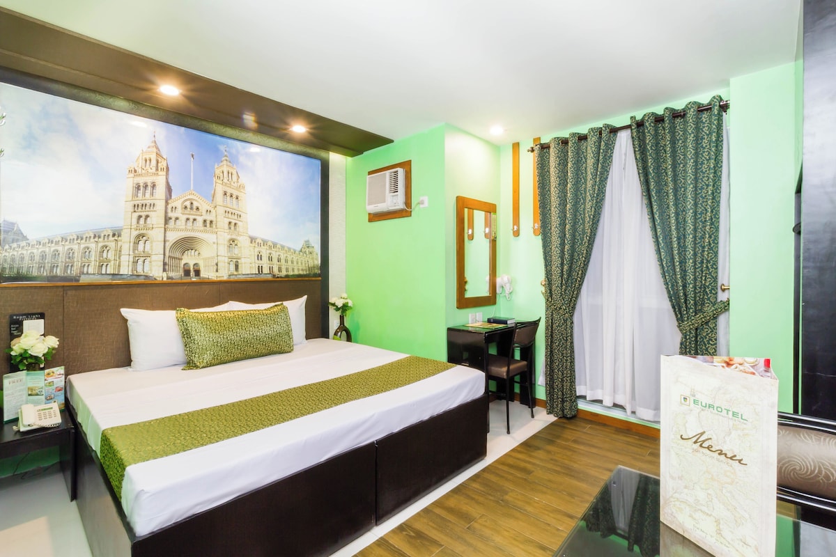 Een hotelkamer met een groot bed, een bureau en uitzicht op een historisch pand.